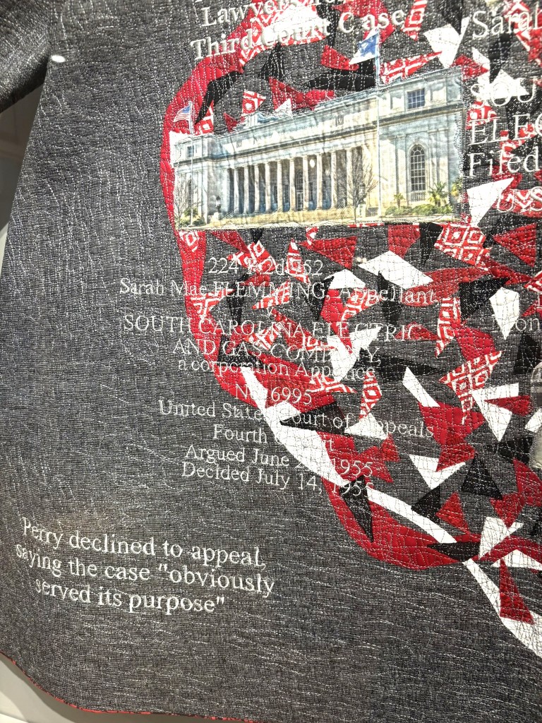 Close up of the coat showing the quilting, lettering (which is court dates and case information for Ms. Flemming), and one of the buildings.  On the bottom left is "Perry declined to appeal, saying the case "obciously served its purpose"